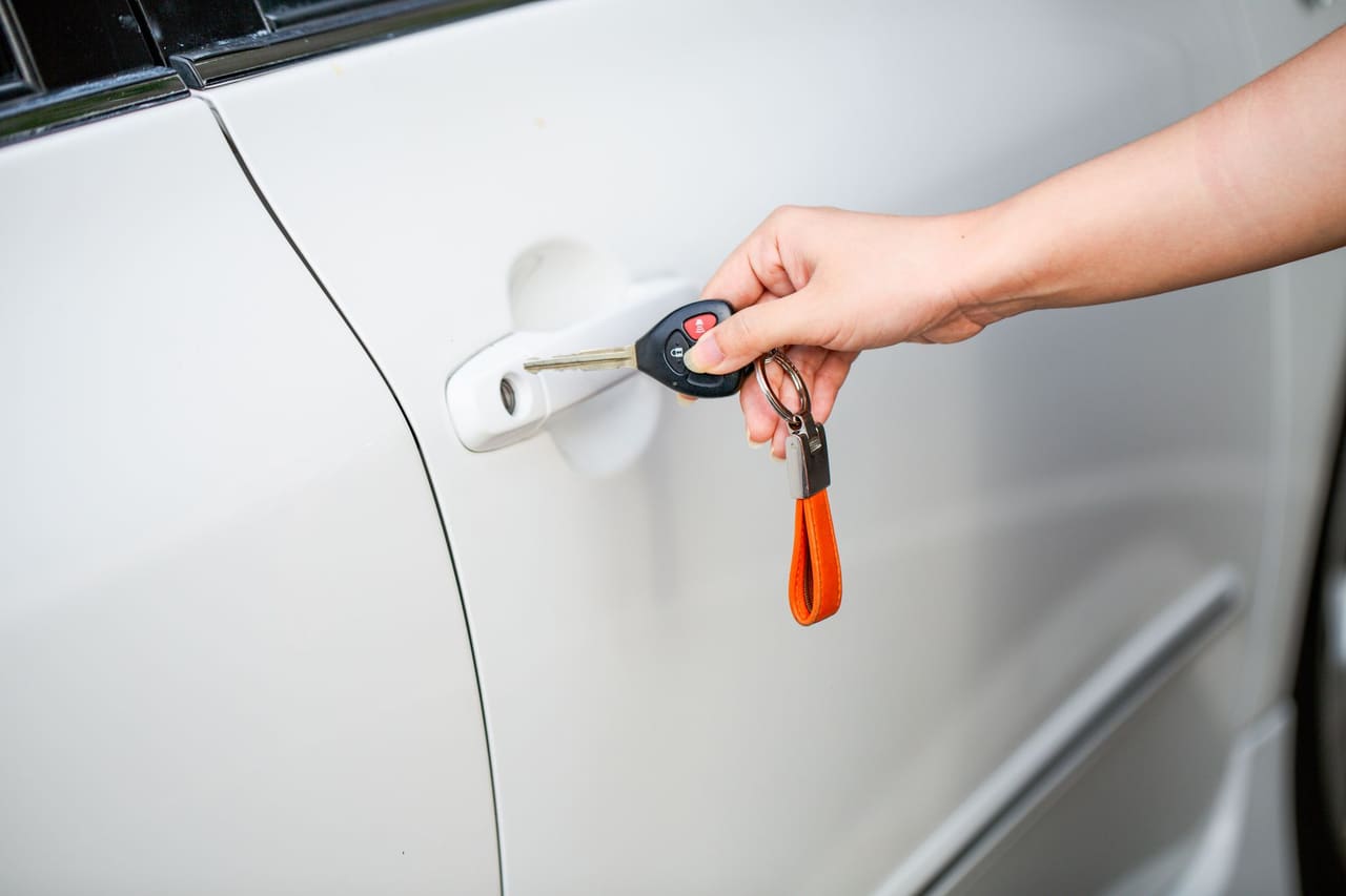 A hand unlocking a car door with the key