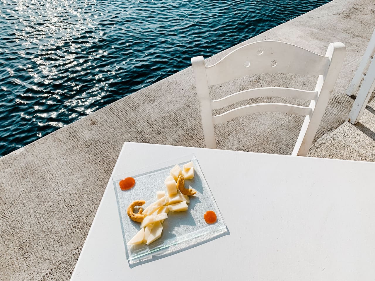 A cheese plate on a white taverna table beside the sea